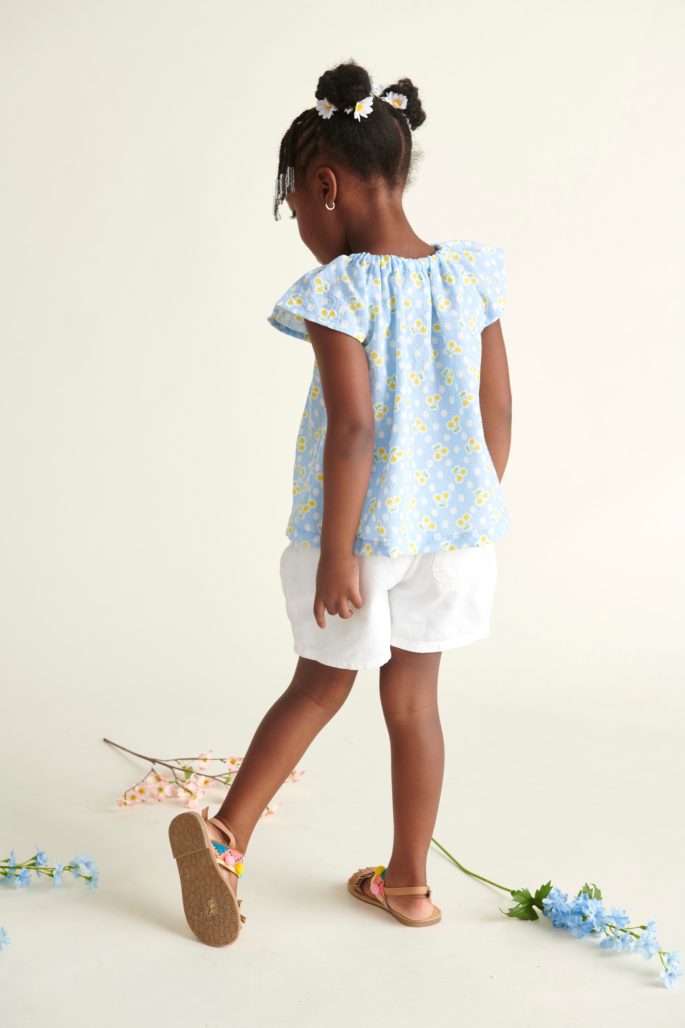 girl wearing summer blouse, blue, yellow cherry print, back