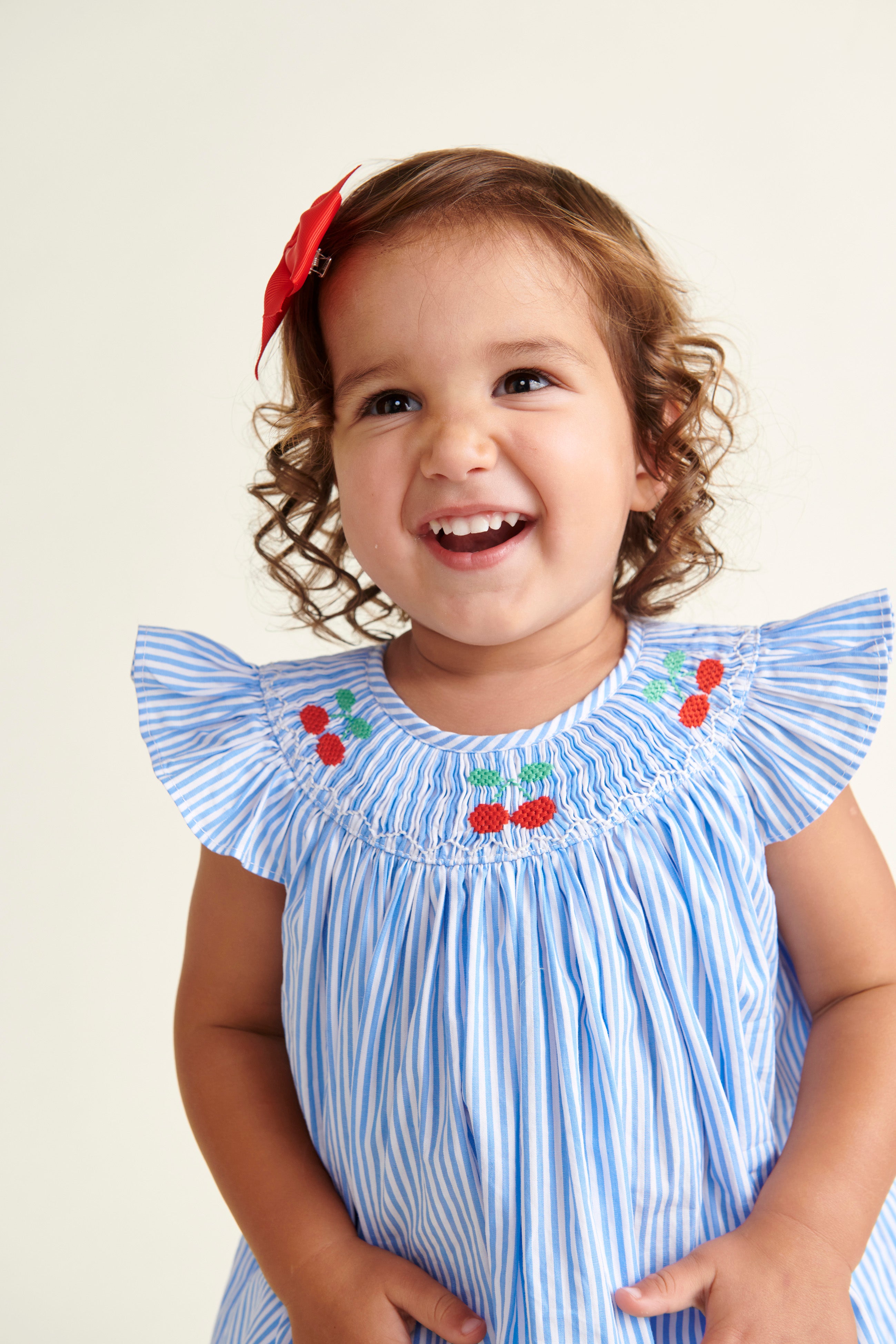 toddler smiling in pinstripe smocked dress with cherry embroidery