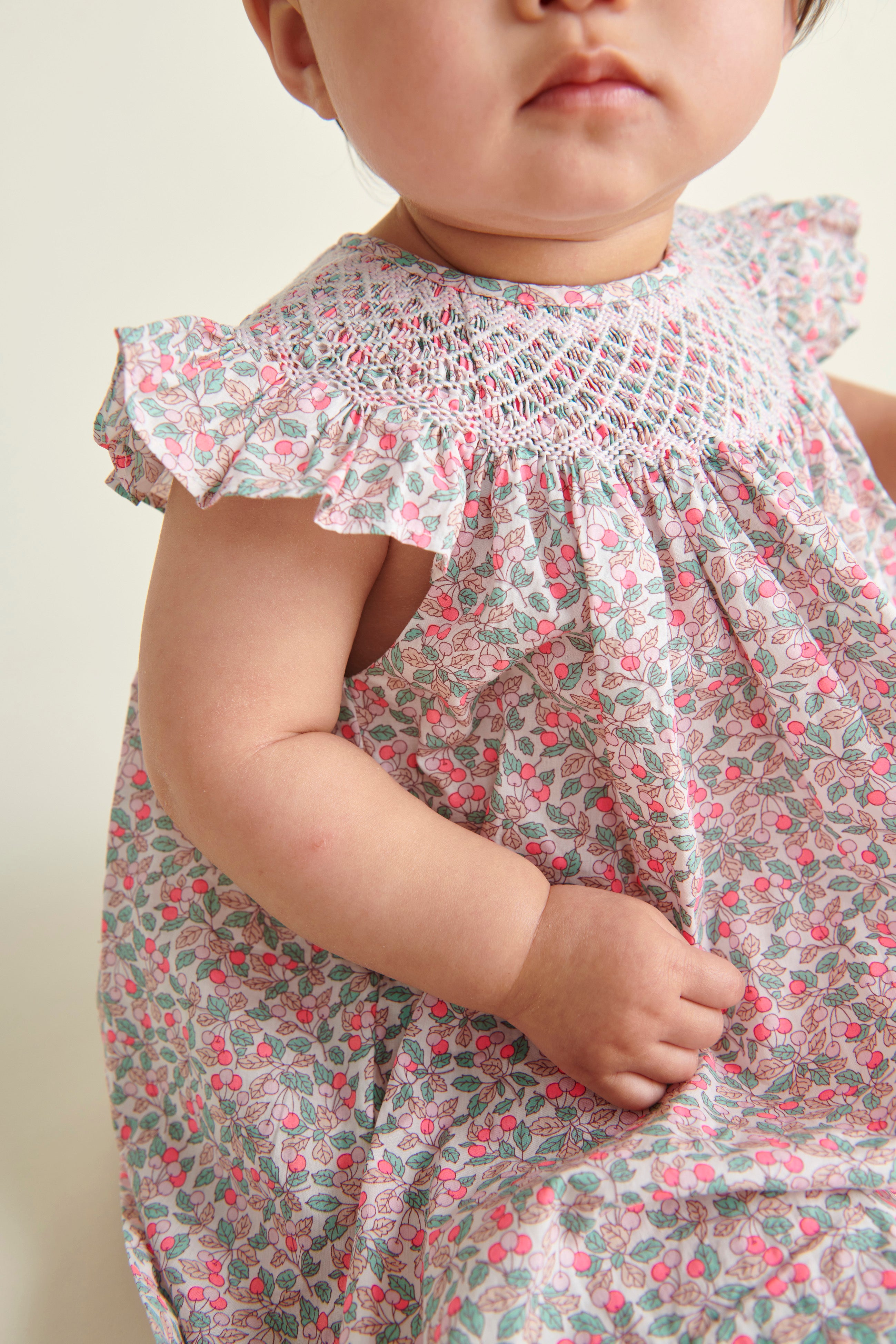 baby model sitting  in hand-smoked Liberty print frill dress, smocking detail shot