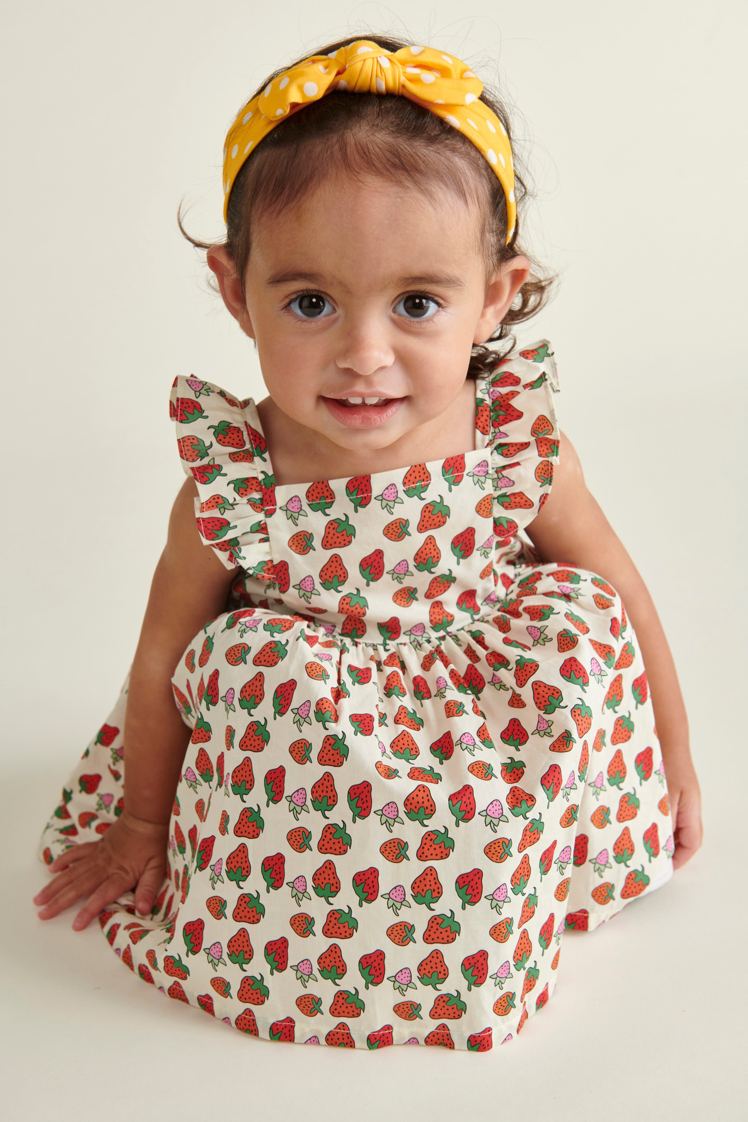 toddler girl i n Strawberry sun dress, crouching