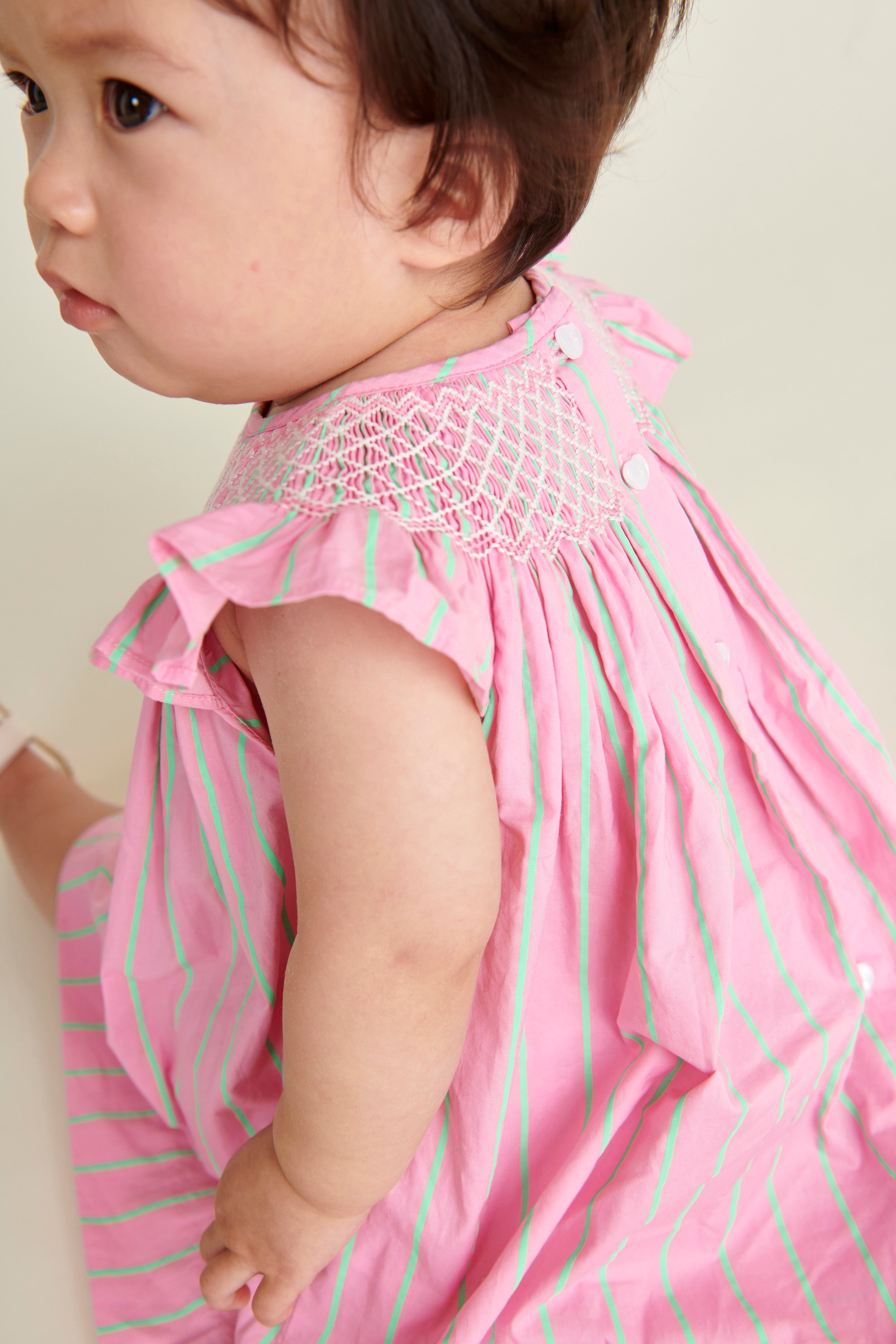 baby in pink  and neon green pinstripe smocked dress, back