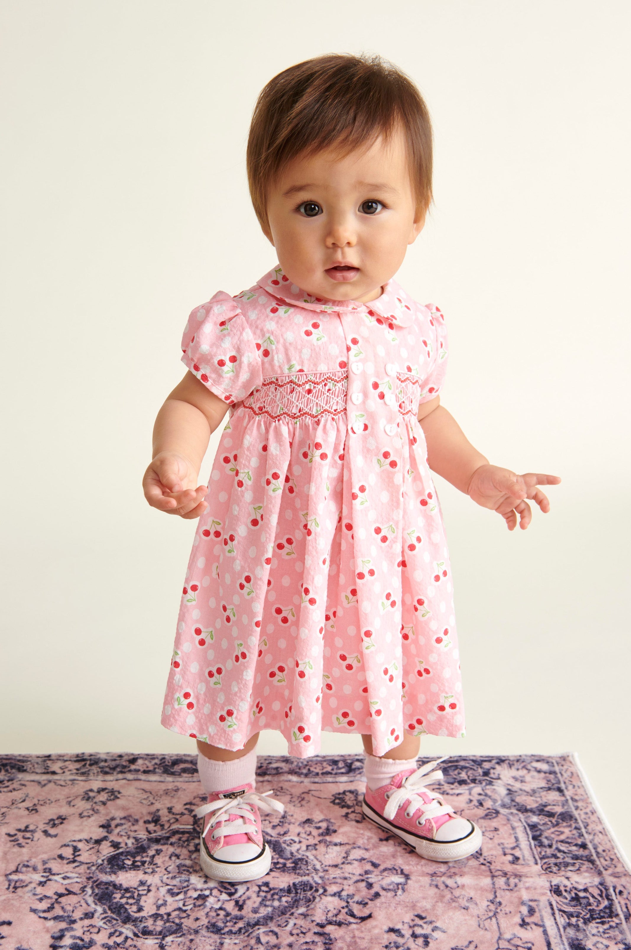 baby in pink hand-smocked dress standing on a rug